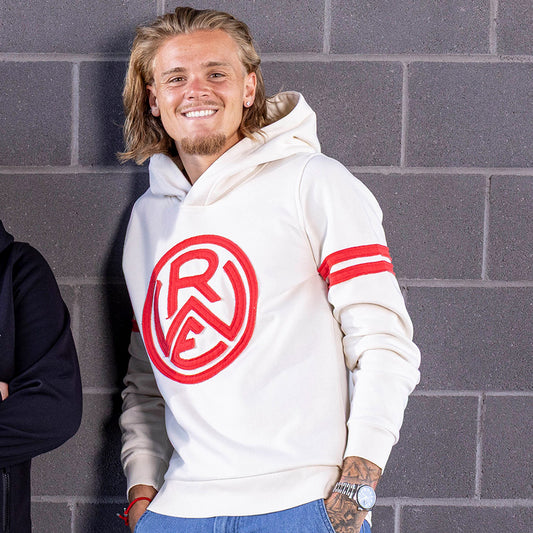 Tom Moustier trägt cremefarbenen Kapuzenhoodie, ohne Kordeln, mit matching Gummi-Patch hinten links auf dem Rippsaum; mit zwei roten Stoffstreifen je Oberarm und großen rotem RWE Stofflogo auf der Brust