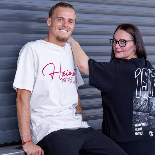 Tom Moustier trägt cremefarbenes Oversize T-Shirt mit einem roten "Heimat seit 1907"-Druck mittig auf der Brust, inkl. Rot-Weiss Essen Logo