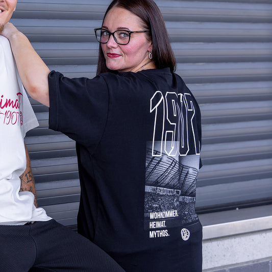 Jasmin trägt schwarzes Oversize T-Shirt mit großem Rückenprint; vorne schlicht mit Koordinaten des Stadions auf der linken Brust