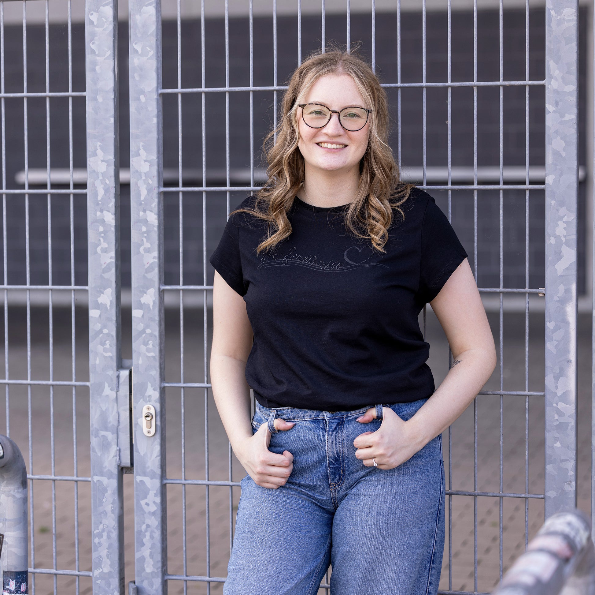 Model trägt schwarzes T-Shirt mit kurzen Ärmel und rotem Nackenband, mit Glitzerdruck und Strass auf der Brust